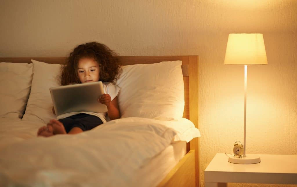 Criança usando o tablet deitada na capa com uma iluminação quente